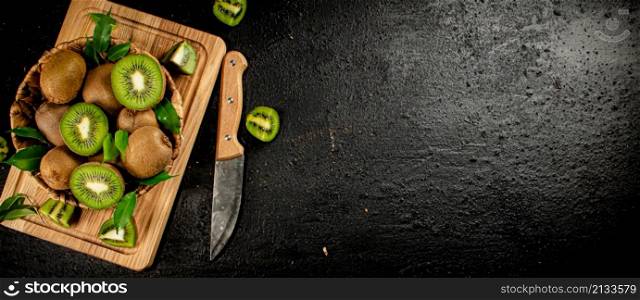 Kiwi in a basket on a wooden cutting board. On a black background. High quality photo. Kiwi in a basket on a wooden cutting board.