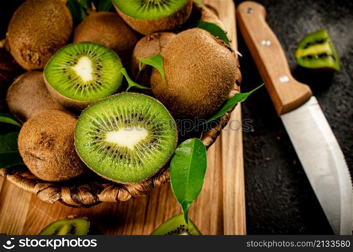 Kiwi in a basket on a wooden cutting board. On a black background. High quality photo. Kiwi in a basket on a wooden cutting board.
