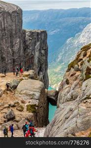 Kjeragbolten, view from the top to the stone stuck between two rocks with fjord in the background and tourists gathered around, Lysefjord, Norway