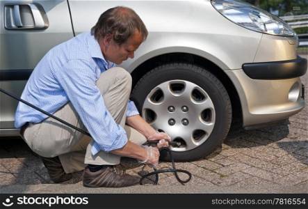 Kneeling man, inflating the right front tyre of his car at a gas station