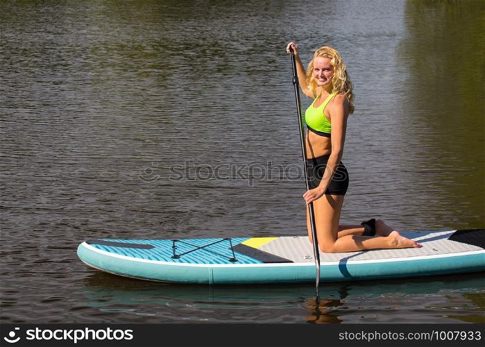 Kneeling young dutch woman paddles with SUP on water of lake