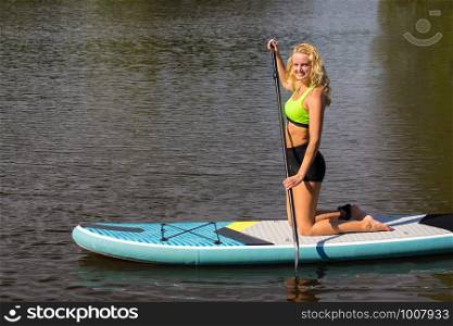 Kneeling young dutch woman paddles with SUP on water of lake