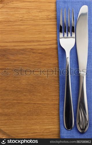 knife and fork at napkin on wooden board