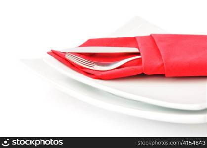 knife and fork in a red napkin on a white double square plate on a white background