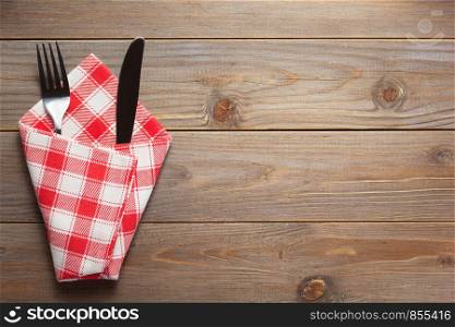 knife and fork in napkin at rustic wooden plank board table background, top view