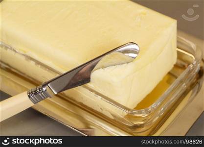 Knife and pack of butter in a butter dish made of metal and glass
