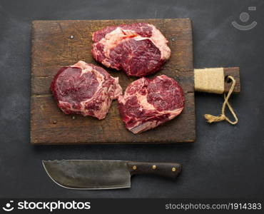 knife and raw piece of beef ribeye on a black table, top view