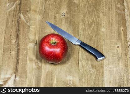 Knife and red apple lie on a wooden surface