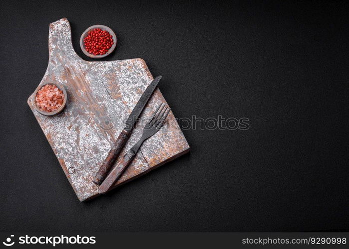 Knife, fork and cutting board, salt, pepper and other ingredients located on a textured concrete background