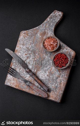 Knife, fork and cutting board, salt, pepper and other ingredients located on a textured concrete background