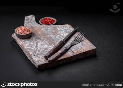 Knife, fork and cutting board, salt, pepper and other ingredients located on a textured concrete background