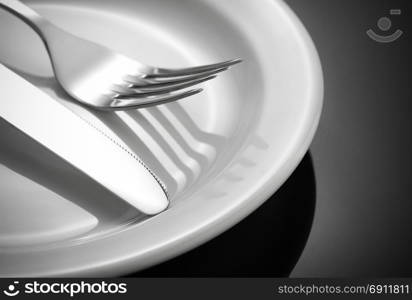 knife, fork and plate at glossy black background