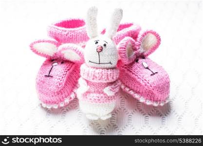 Knitted pink baby booties with rabbit muzzle and toy over textile background