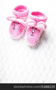 Knitted pink baby booties with rabbit muzzle over textile background