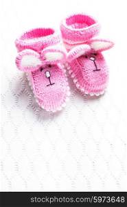Knitted pink baby booties with rabbit muzzle over textile background. Knitted baby booties