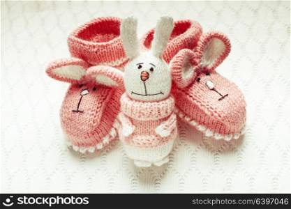 Knitted pink baby booties with rabbit muzzle over textile background. Knitted baby booties