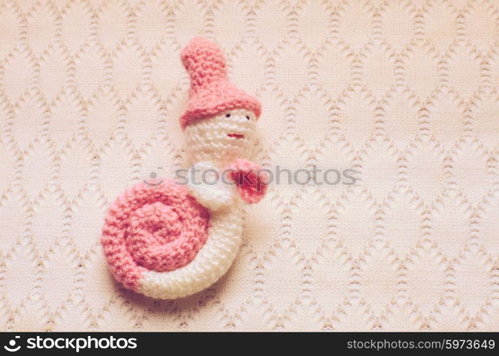 Knitted white with pink snail hung on the wall. Decorative crochet snail