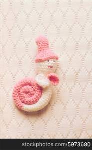 Knitted white with pink snail hung on the wall. Decorative crochet snail