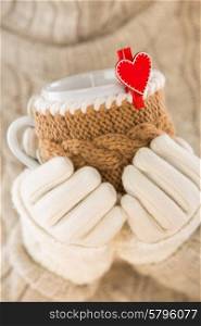 Knitted wool cup in human hands. With red hearts and the word love.