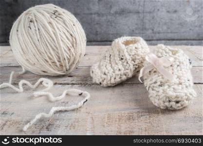 Knitting baby booties with bege yarn on wooden table
