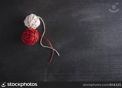 Knitting concept with red and white cotton coils on a black background. Above view of two thread balls. Flat lay of winter indoor activities.