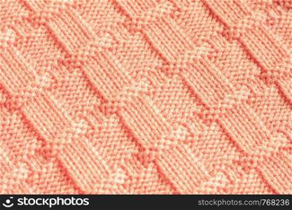 Knitting fabric made of wool yarn peach color with geometric pattern. knitted cloth needles, handmade. Background, texture.