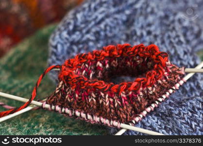 Knitting with red wool on grey knitting needles on white