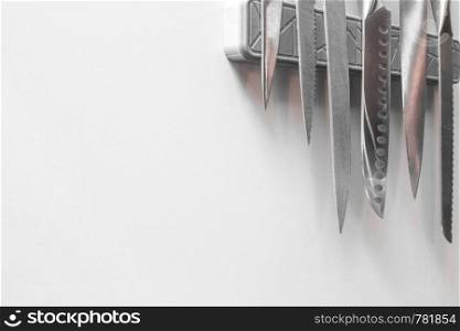 Knives on magnetic wall support in a kitchen on white wall, space for text clean and modern. Knives on magnetic wall support in a kitchen on white wall, space for text