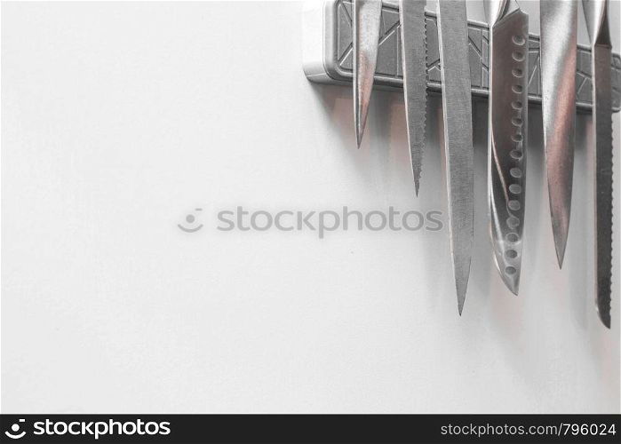 Knives on magnetic wall support in a kitchen on white wall, space for text clean and modern. Knives on magnetic wall support in a kitchen on white wall, space for text