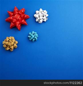 knotted multi-colored ribbon bows on a blue background, top view, copy space