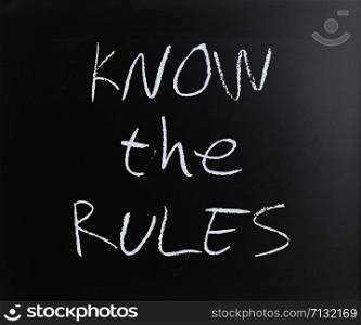 ""Know the rules" handwritten with white chalk on a blackboard."