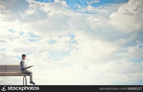 Knowledge advantage. Young man in casual sitting on bench with book in hands