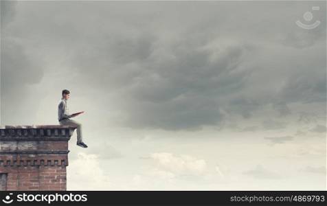 Knowledge advantage. Young man in casual sitting on building top with book in hands