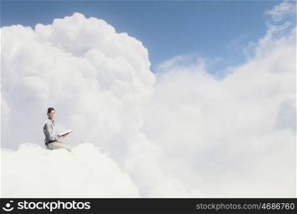 Knowledge advantage. Young man in casual sitting on cloud with book in hands