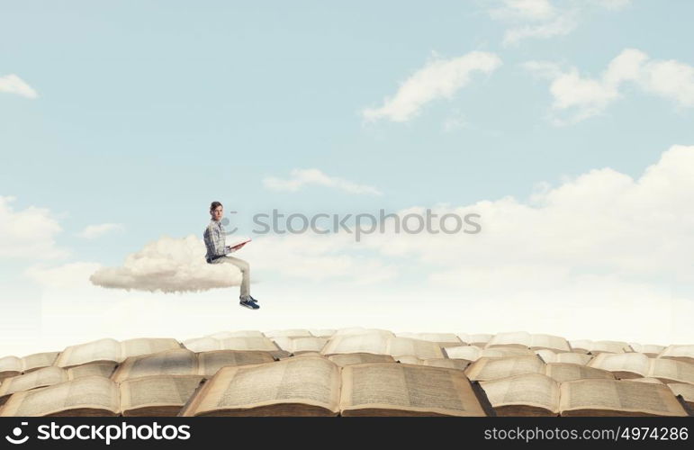 Knowledge advantage. Young man in casual sitting on cloud with book in hands