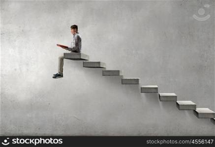 Knowledge advantage. Young man in casual sitting on ladder steps with book in hands