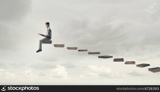 Knowledge advantage. Young man in casual sitting on ladder steps with book in hands