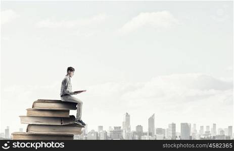 Knowledge advantage. Young man in casual sitting on pile of old books