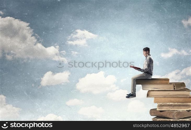 Knowledge advantage. Young man in casual sitting on pile of old books