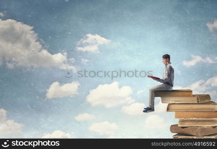 Knowledge advantage. Young man in casual sitting on pile of old books