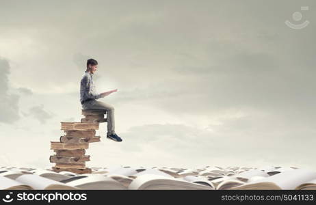 Knowledge advantage. Young man in casual sitting on pile of old books