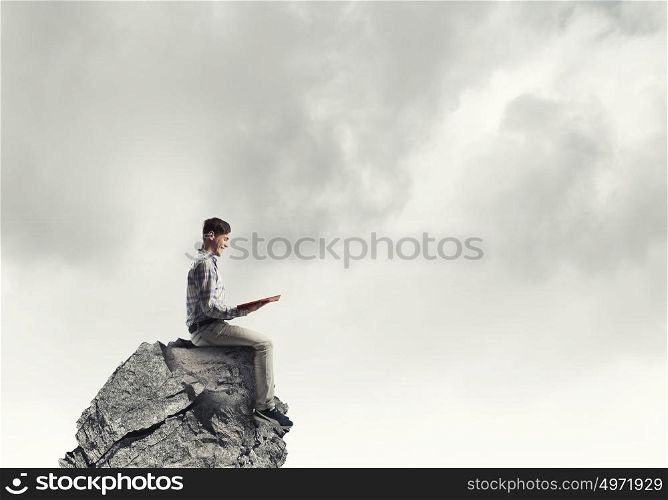 Knowledge advantage. Young man in casual sitting on rock top with book in hands