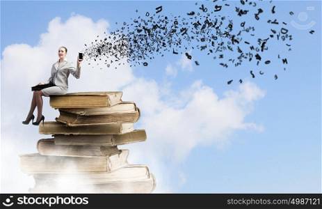Knowledge advantage. Young woman in suit sitting on pile of old books