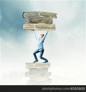 Knowledge and education. Young man holding huge book above head
