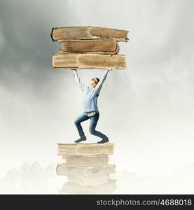 Knowledge and education. Young man holding huge book above head