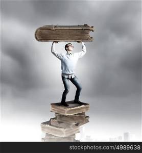 Knowledge and education. Young man holding huge book above head