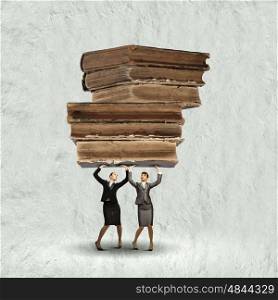 Knowledge concept. Two young ladies lifting pile of old books above head