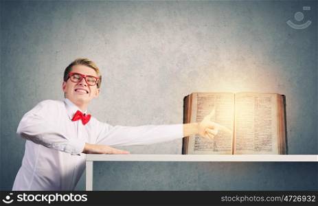 Knowledge concept. Young man in glasses pointing at opened book