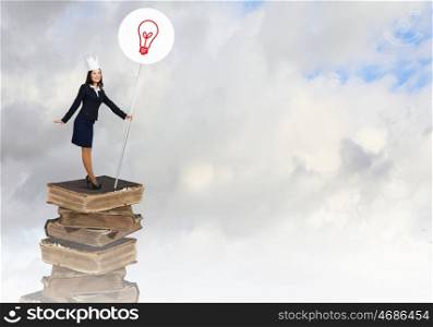 Knowledge is power. Young businesswoman in paper crown standing on pile of books