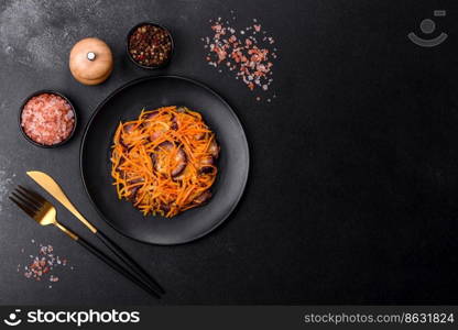 Korean salad with carrots and aubergine in a plate with garlic, black textured background. Korean salad with eggplant, carrots, garlic, spices and herbs on a dark concrete background